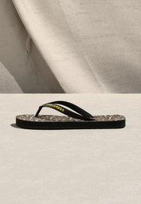 Sandale tong avec des brides noires ornées du texte jaune "Dsquared2" et une semelle imprimée léopard, sur un fond neutre.