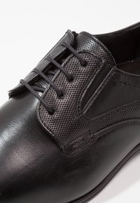 Chaussure habillée en cuir noir avec un panneau en maille texturée, bout rond et design classique à lacets. Fini lisse avec des détails de couture subtils.