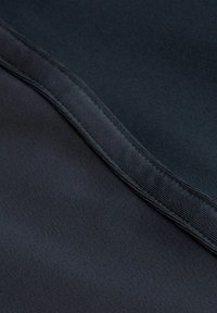 Közelkép sötét szövetből, sima textúrával, egy átlósan futó varrással a keret mentén.