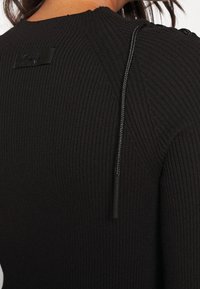 Pull noir côtelé avec un col montant, des boutons latéraux, une finition texturée et un cordon décoratif à l'épaule.