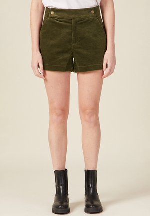 Olijfgroene corduroy shorts met een hoge taille, voorzakken en twee decoratieve knopen. Gecombineerd met zwarte enkellaarsjes.
