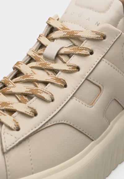 Κοντινή λήψη μπεζ δερμάτινου αθλητικού παπουτσιού με κορδόνια σε μπεζ και λευκό σχέδιο και παχύ υφασμάτινο πέλμα.