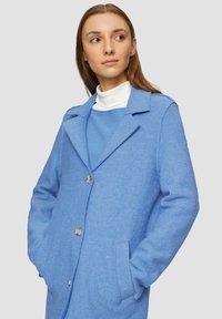 Cappotto in misto lana azzurro chiaro con collo a lancia, bottoni frontali e tasche laterali. Presenta una vestibilità rilassata e una texture morbida.