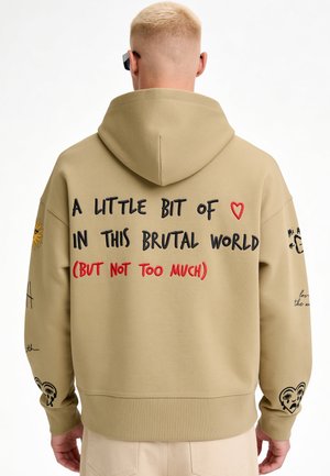 Sweat à capuche beige avec un texte noir et rouge indiquant « "A little bit of love in this brutal world (but not too much)" », porté par une personne de dos.