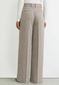 Laiade säärtega püksid struktuurse pruuni kangaga, millel on peen muster. Omadusteks on vöökoht, tagataskud ja kohandatud lõige.