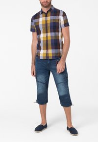 Short-sleeve plaid shirt in blue, yellow, and white with a chest pocket. Worn with knee-length denim cargo shorts featuring side pockets.