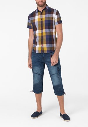 Kurzärmliges kariertes Hemd in Blau, Gelb und Weiß mit einer Brusttasche. Getragen mit knielangen Jeans-Cargo-Shorts mit Seitentaschen.