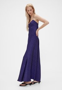 Lila Slip-Kleid mit weißen Punkten, Spaghettiträgern und fließender Silhouette. Verfügt über einen ausgestellten Saum und wird mit schwarzen flachen Sandalen kombiniert.