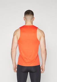 Top sin mangas rojo hecho de una tela suave y elástica, con un escote redondeado y costuras planas, combinado con leggings deportivos negros.