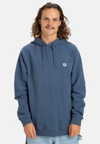 Sudadera azul hecha de un tejido suave con un bolsillo tipo canguro, capucha ajustable con cordón y puños acanalados. Presenta un pequeño logo en el pecho.
