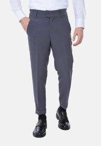 Pantaloni grigi con un design sartoriale, pieghe frontali e orli rifiniti. Abbinati a mocassini neri e una camicia bianca.