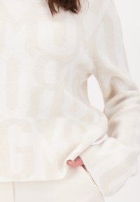 Crèmekleurige sweater van zachte stof, met een groot, subtiel letterpatroon, geribbelde manchetten en een relaxte pasvorm.