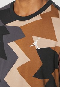 Koszulka z krótkim rękawem wykonana z mieszanki bawełny, z geometrycznym wzorem w odcieniach brązu, beżu i czerni oraz z małym białym logo na klatce piersiowej.
