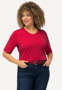 Rode T-shirt met korte mouwen en V-hals, gemaakt van een gladde stof, gecombineerd met donkerblauwe spijkerbroek en een gestreepte riem met rode en zwarte accenten.