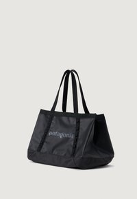 Geantă de tip tote de culoare neagră, fabricată dintr-un material durabil, având un design spațios, două mânere împletite și un logo subtil pe față.