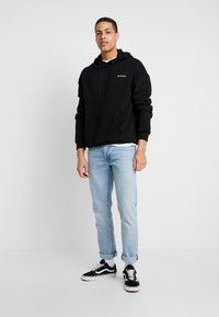 Black hooded sweatshirt with front pocket, gray text logo, light blue jeans, and black sneakers with white soles. Simple, casual design.