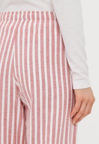 Red and white striped wide-leg pants with elastic waistband, made of soft fabric, showing a portion of a white long-sleeve top and a hand.