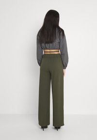 Zkrácená šedá bunda s elastickým lemem, spárovaná s olivově zelenými kalhotami s vysokým pasem a širokými nohavicemi. Hladká textura a volný střih.