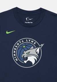 T-shirt en coton bleu marine arborant le logo des Minnesota Lynx avec un puma gris et blanc, un ballon de basket et des accents étoilés verts. Logo Nike inclus.