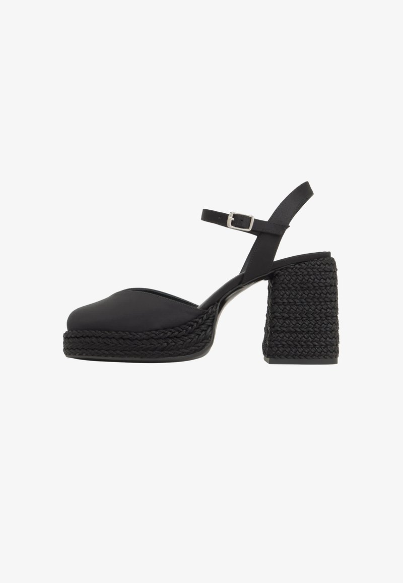 Sandale à plateforme noire avec talon tressé épais et bride de cheville avec petite boucle argentée, présentée de profil sur fond blanc.