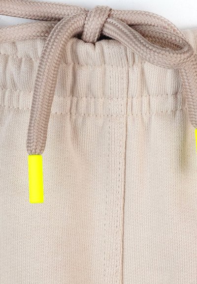 Joggers bej din tricot, cu un brâu elastic, având șnur împletit și vârfuri de un galben neon. Material texturat și moale, cu cusături vizibile.