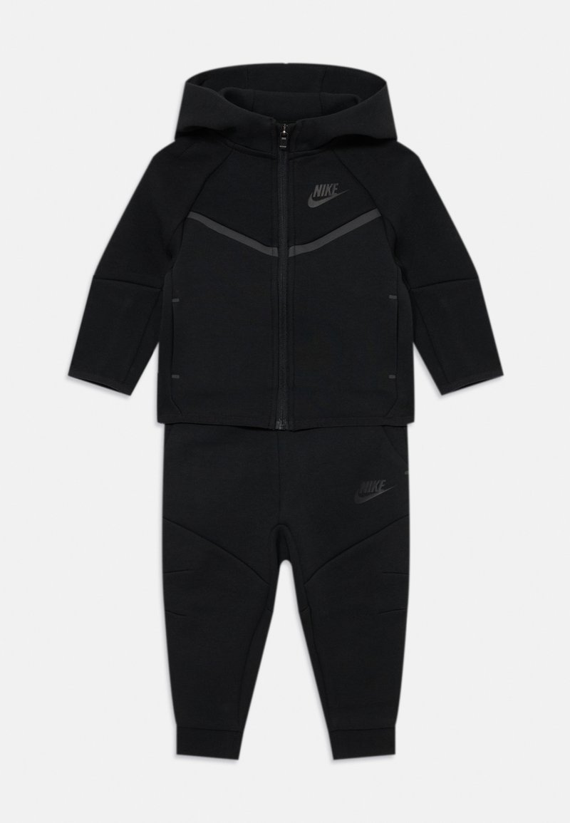 Tuta Nike nera con cappuccio, zip frontale e accenti grigi a contrasto, pantaloni aderenti con dettagli sui pannelli delle ginocchia.