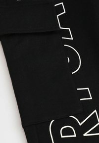 Czarna tkanina bawełniana z białym nadrukowanym wzorem. Szczegóły obejmują złożoną sekcję wzdłuż krawędzi oraz kontrastowy wzór graficzny.