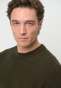 Olivgrön ribbad stickad tröja med rund halsringning, med en strukturerad yta och en figurnära silhuett.