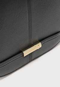 Μαύρη δερμάτινη τσάντα χειρός με υφή στην επιφάνεια, διαθέτει χρυσό κούμπωμα και κομψό σχέδιο με ραφές.