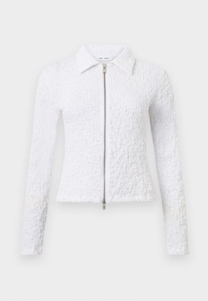 Veste blanche à manches longues texturée avec col et fermeture éclair argentée bidirectionnelle, coupe ajustée, présentée sur fond uni.