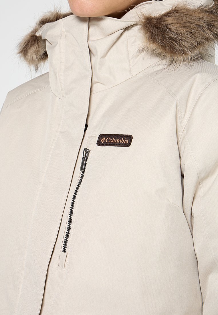 Beige Außenjacke mit Kunstfellbesatz an der Kapuze, Reißverschlussfronttasche und Columbia-Logo-Patch auf der Brust. Wasserabweisendes Material.