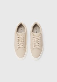 Beige tossud sileda, tekstuuriga pinnaga, ümarate varvaste ja valgete detailidega. Omab kinganöörid ja brändi silt sees.