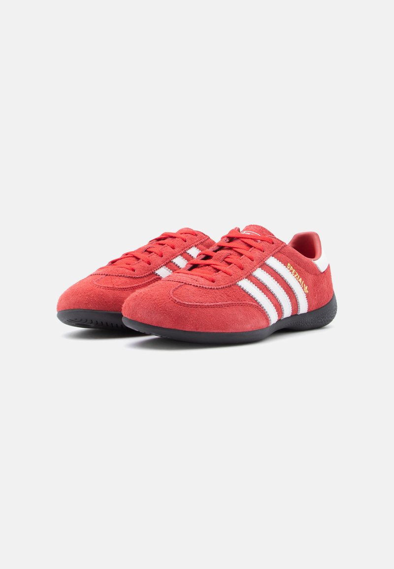 Red suede sneakers with white stripes, flat black rubber soles, and round laces. Features a gold "Spezial" accent on the side.