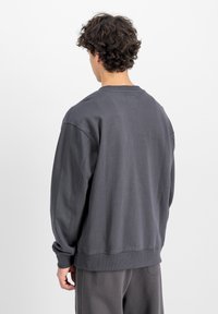 Mörkgrå oversized sweatshirt med rundad halsringning, ribbad muddar och en etikettdetalj på baksidan. Mjuk textur, enkelt design och avslappnad passform.