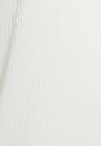 Tissu blanc avec un motif de grille texturé subtil, montré en gros plan avec de légers plis et des ombres douces.