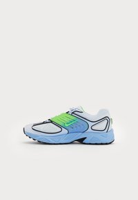 Chaussures de sport avec une tige en mesh blanche et bleu clair, des accents noirs et des touches de vert, une semelle texturée et un design épuré.