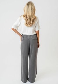 Sive široke hlače z elastičnim pasom in dvema zadnjima žepoma, v kombinaciji z belo majico s kratkimi rokavi, prikazane s hrbtne strani.