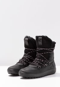 Bottes d'hiver noires avec une surface texturée, une doublure en fausse fourrure, une semelle en caoutchouc épaisse et des lacets tressés avec de subtils accents blancs.