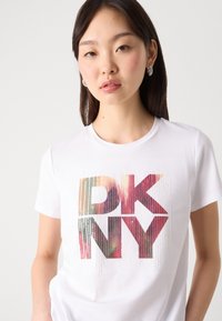 Weißes T-Shirt mit kurzen Ärmeln, das ein farbenfrohes "DKNY"-Grafikdesign präsentiert. Aus weichem Baumwollmaterial mit rundem Ausschnitt und lockerem Schnitt.
