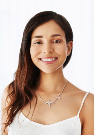 Collana in argento con design a onda di battito cardiaco e piccolo ciondolo a forma di cuore, indossata su un top bianco a coste. La catena è delicata e lucente.