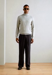 Pulover gri cu guler înalt, textură cu reia, asociat cu pantaloni negri cu dungi fine și pantofi negri. Modelul poartă ochelari de soare, stând în fața unui fundal neutru.
