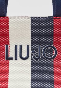 Sac fourre-tout en tissu rayé aux couleurs rouge, blanc et marine. Présente un logo "LIU•JO" brodé en fil foncé. Surface texturée, poignées robustes.