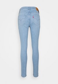 Jeans ajustados de color azul claro vistos desde la parte de atrás, con dos bolsillos traseros, presillas para cinturón y una pequeña etiqueta de tela roja en el bolsillo derecho.