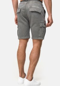 Shorts cargo en denim gris avec une coupe décontractée, dotés de plusieurs poches utilitaires et d'une taille plate, associés à des baskets blanches.