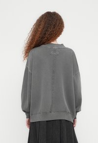 Γκρίζο υπερμεγέθες φούτερ με στρογγυλή λαιμόκοψη, κατεβασμένους ώμους, ραφή στην πλάτη και ριμπ τελείωμα, συνδυασμένο με μαύρη φούστα.