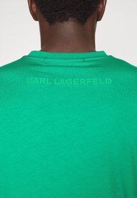 Zielona bawełniana koszulka z okrągłym dekoltem i wytłoczonym napisem "KARL LAGERFELD" z tyłu. Gładka tekstura z jednolitym wzorem.