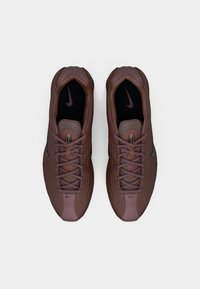 Nike sportcipő barna és bordó színben, hálós felsőrésszel, kerek orral és lapos fűzővel. Fekete belső talppal rendelkezik, és diszkrét logó részlet van rajta.