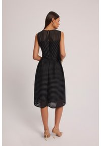 Czarna sukienka w poziome paski, bez rękawów, do kolan, z otworem w tylnej części. Gładka tekstura z subtelną przezroczystością.