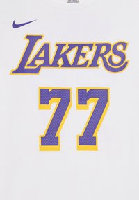 Vit T-shirt med lila "LAKERS" text och guldkant; fet lila nummer "77" med prickig textur och gula accenter. Nike-logotyp högst upp till vänster.