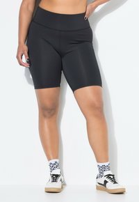 Zwarte hoogmontage fietsbroek van rekbare stof, met een gladde textuur en een aansluitend ontwerp. Gepaard met witte sneakers en gestreepte sokken.